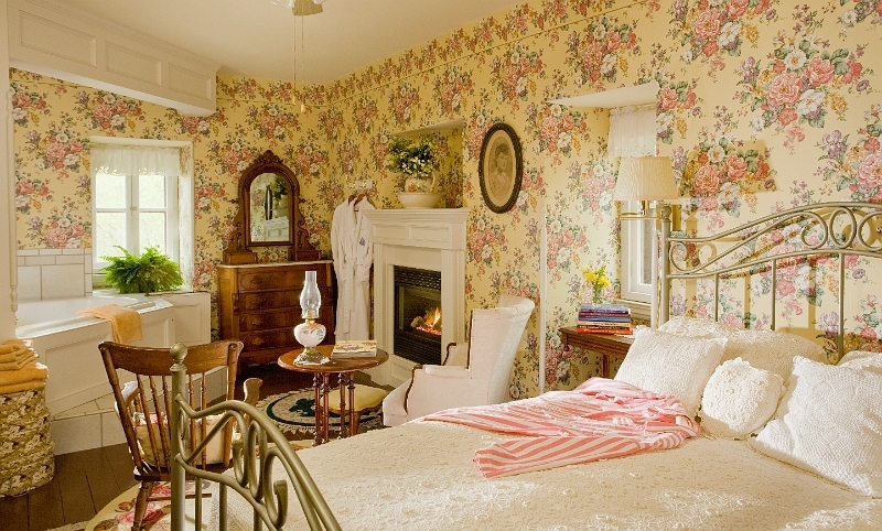 A bedroom with a large bed, a fireplace, a jacuzzi tub, and floral wallpaper.