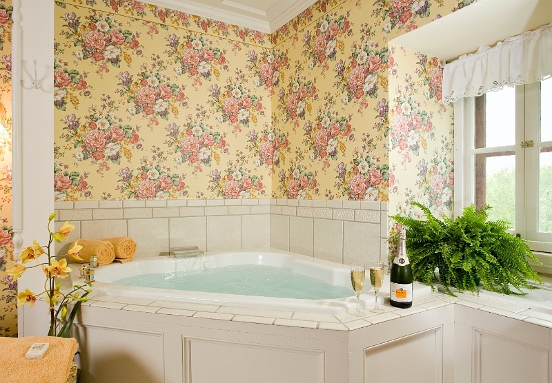 A relaxing bathroom with a corner bathtub, a window, and floral wallpaper.