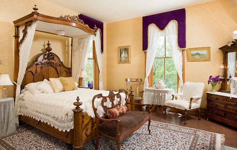 A luxurious bedroom with a canopy four-poster bed, a plush bench, and elegant furnishings.