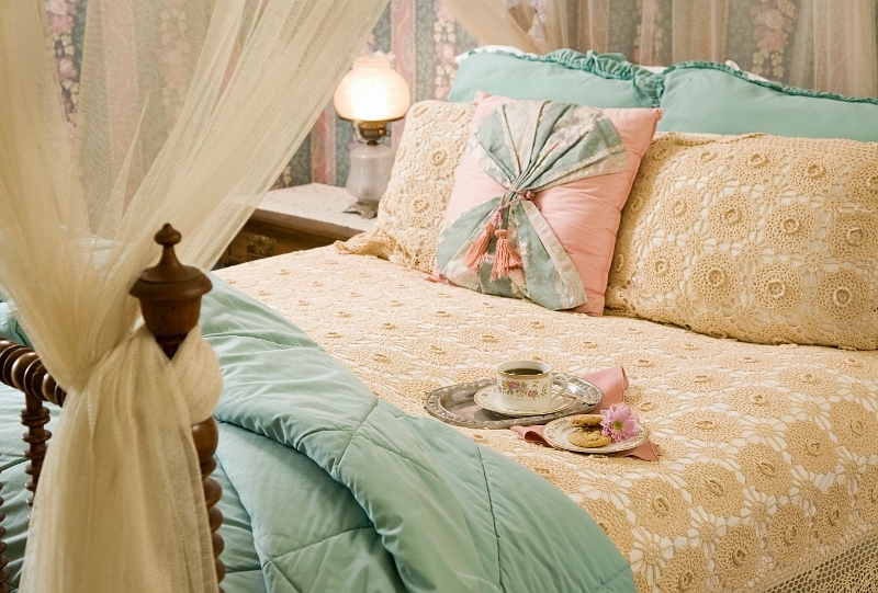 A cozy bed with a white canopy, decorative pillows, and a tray with a cup and saucer, perfect for a leisurely breakfast.