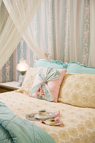 A cozy bed with a white canopy, decorative pillows, a bedside lamp, and a tray with a cup and saucer.