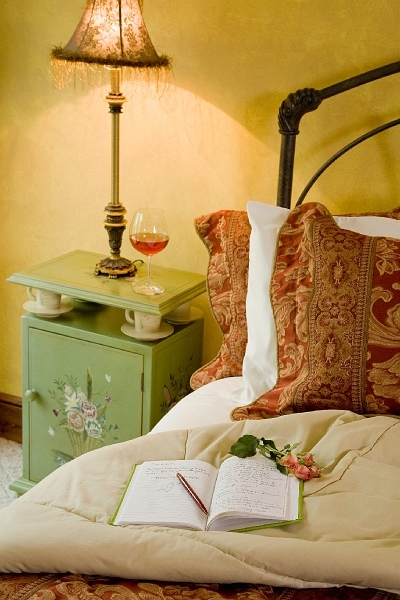 A romantic bedside scene with a lamp, a glass of wine, a journal, and a rose, inviting relaxation and contemplation.