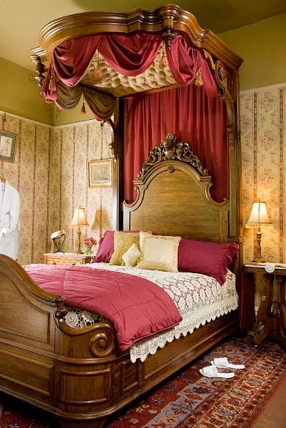 A romantic bedroom with a large four-poster bed with a canopy, a bedside table with a lamp, and a rug on the floor.