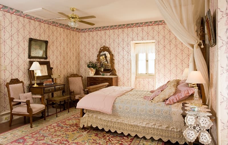 A cozy bedroom with a four-poster bed, a desk with a chair, and a patterned rug.