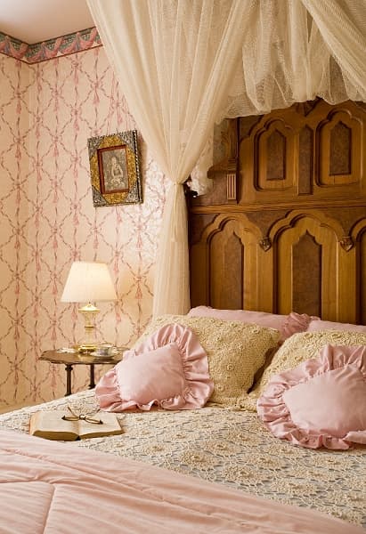 A romantic bed with a white canopy, ruffled pink pillows, and a book on the bed.