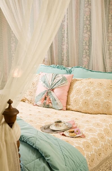 A cozy bed with a white canopy, decorative pillows, a bedside lamp, and a tray with a cup and saucer.