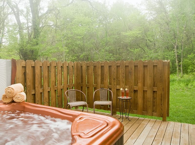 A private hot tub oasis with a wooden fence and comfortable seating, perfect for relaxation in a peaceful outdoor setting.