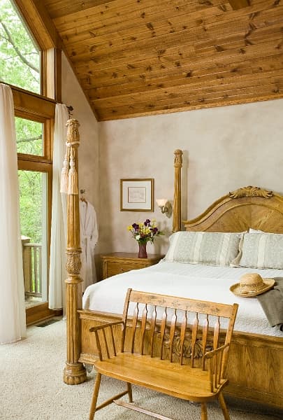 A bedroom with a large bed, a window overlooking a balcony, and a wooden bench at the foot of the bed.