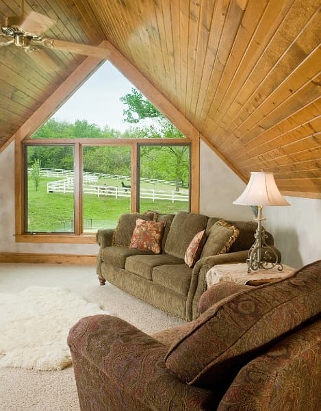 A relaxing sitting area with a vaulted ceiling, a large window with a view of nature, and plush seating.
