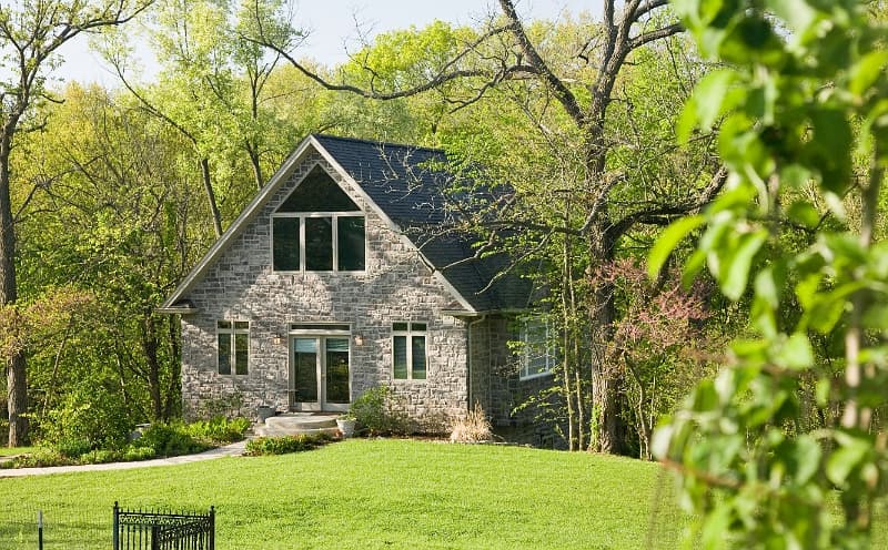 A charming stone house with a unique architectural style, surrounded by mature trees and a well-maintained lawn.