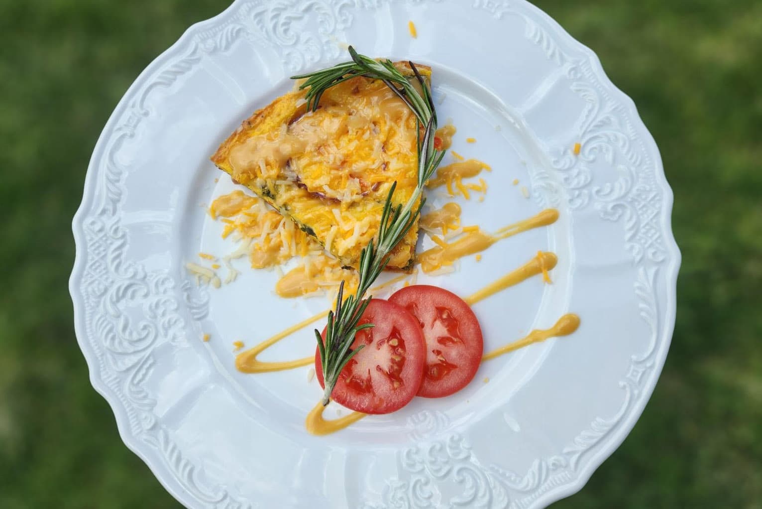 A savory quiche garnished with rosemary and served with fresh tomato slices presented beautifully on a white plate.