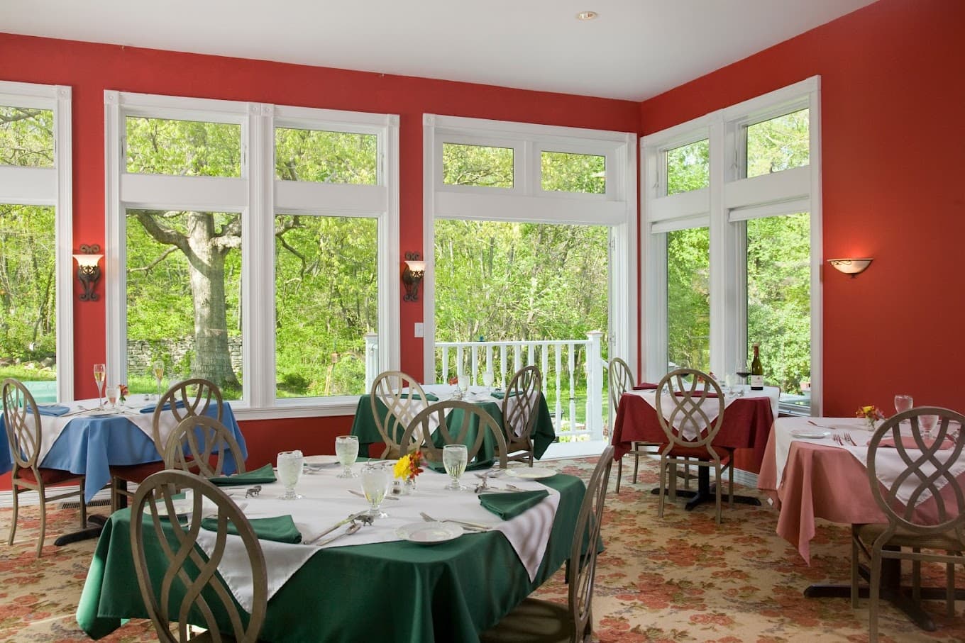 Bright restaurant with large windows and elegantly set tables in a shades of blue, green, and red.