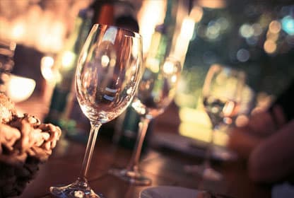 A close-up shot of empty wine glasses on a warmly lit dining table creates an inviting, elegant atmosphere.