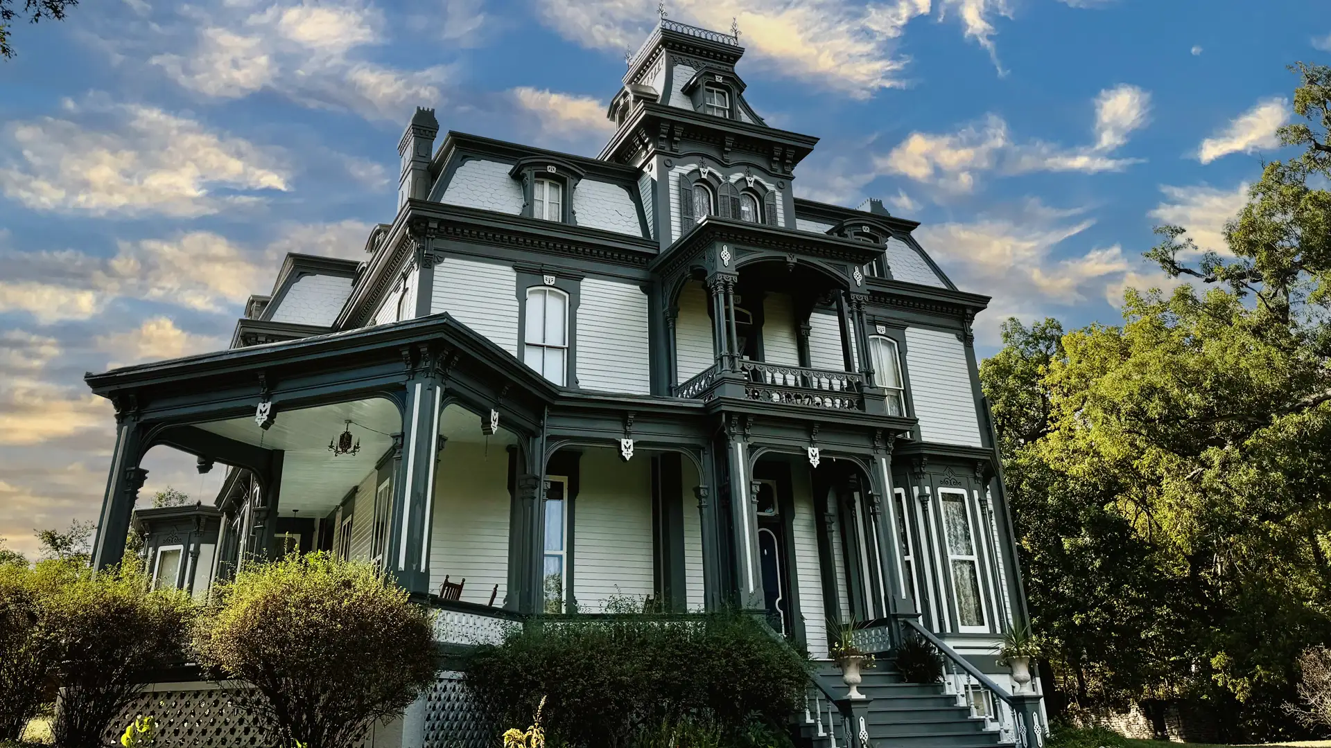 Garth Woodside Mansion is a grand Victorian house with intricate detailing, multiple balconies, and a wraparound porch set against a clear sky and greenery.